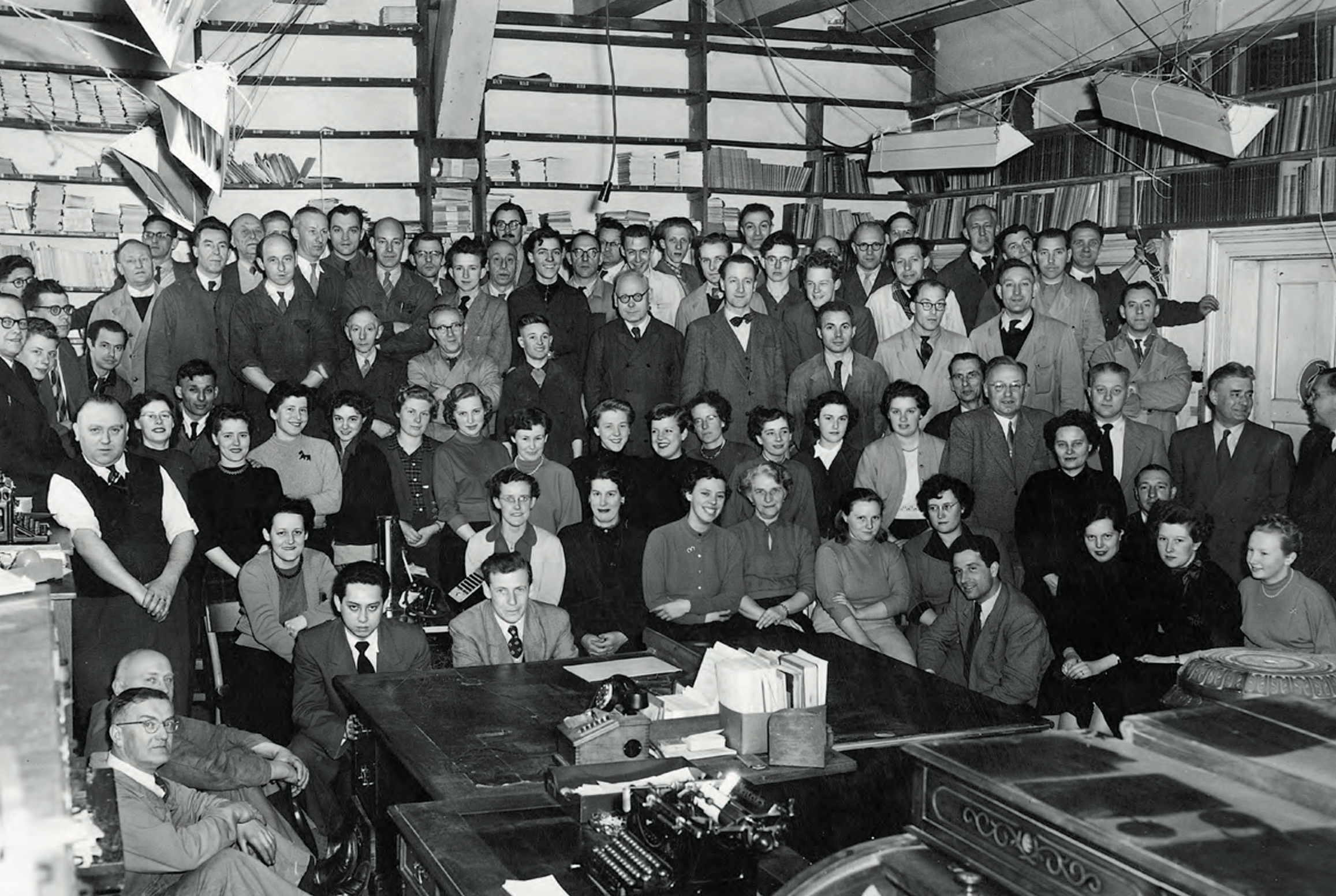Schwarz-Weiß-Fotografie von etwa neunzig Personen, die für ein Foto posieren, wobei die Frauen im Vordergrund sitzen