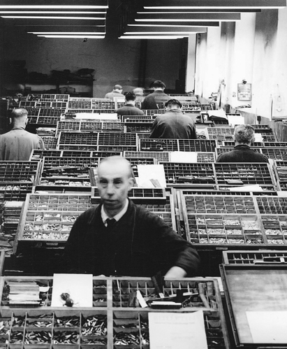 Black and white photograph of a room full of type cases and several men at work on them